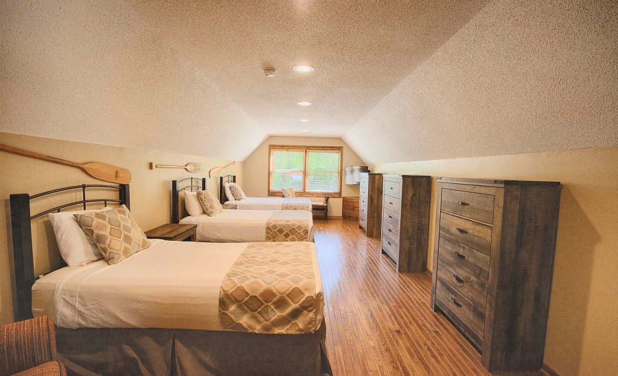 a room with a three single beds each facing towards a wooden storage drawer along with a window in the far end of the room - Historic Tapoco Lodge