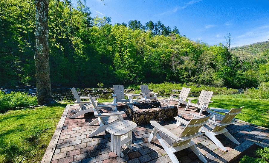an outdoor seating area with a fire pit in the middle surrounded by wooden chairs amidst lush greenery - Historic Tapoco Lodge