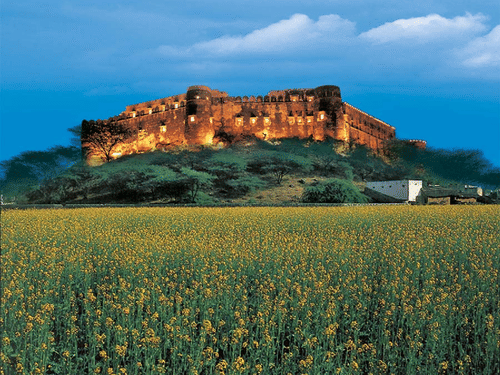 The facade of Hill Fort Kesroli Kesroli with grass at the forefront and blue sky in the background.
