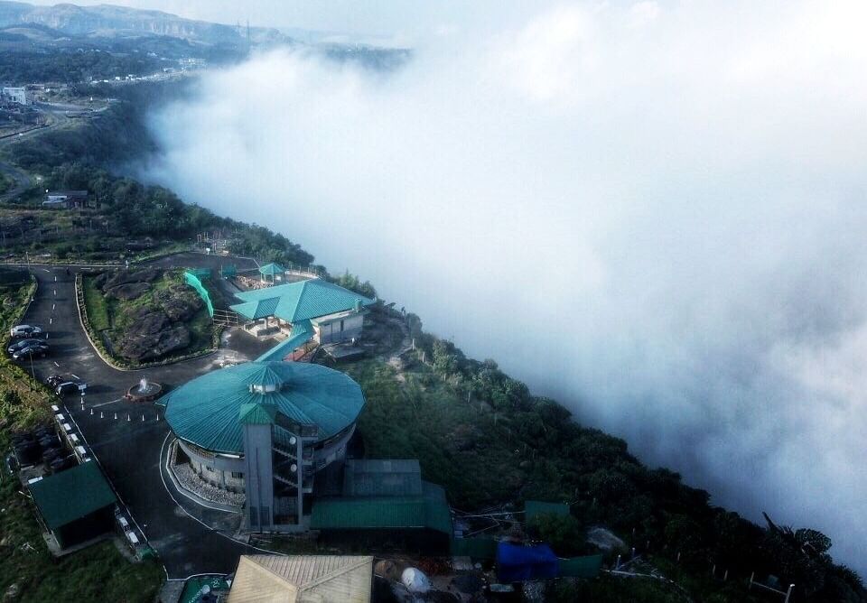 Aerial view of Polo Resort Cherrapunjee surrounded by clouds and green landscape.
