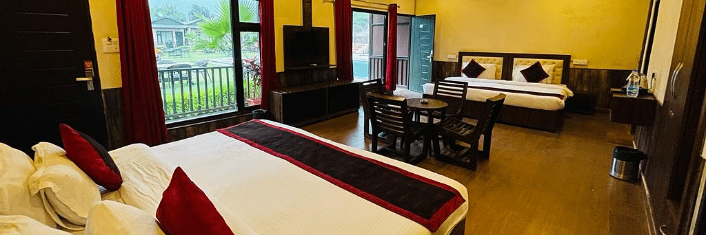 A Family Cottage with beds facing towards each other seperated by a round dining table and TV at DLS MJ River Resort, Rishikesh.