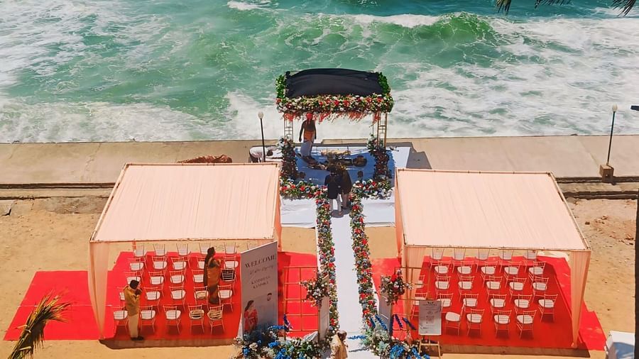 An image of a beachfront wedding setup with a floral arch, chairs neatly arranged on a red carpet, and a scenic ocean backdrop