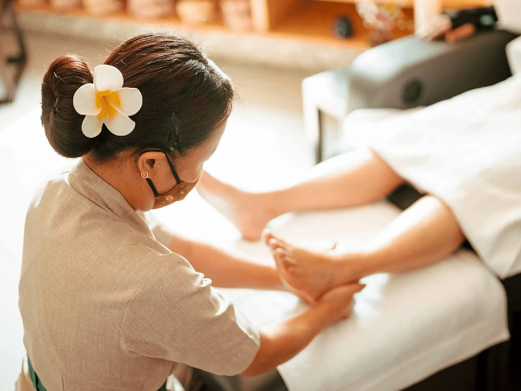 Spa therapist giving a leg massage to a client lying on a white massage bed with wooden shelves in the background at Karma Chalets.