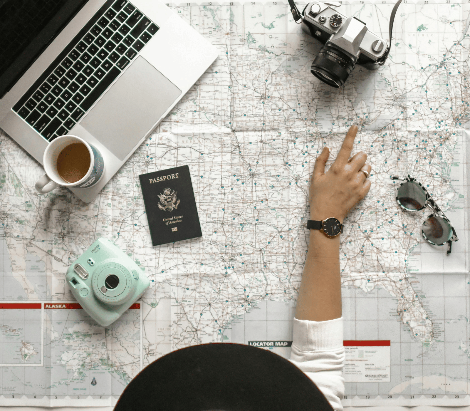 Top view of a workspace with travel essentials, including a laptop, map, camera, and coffee cup.