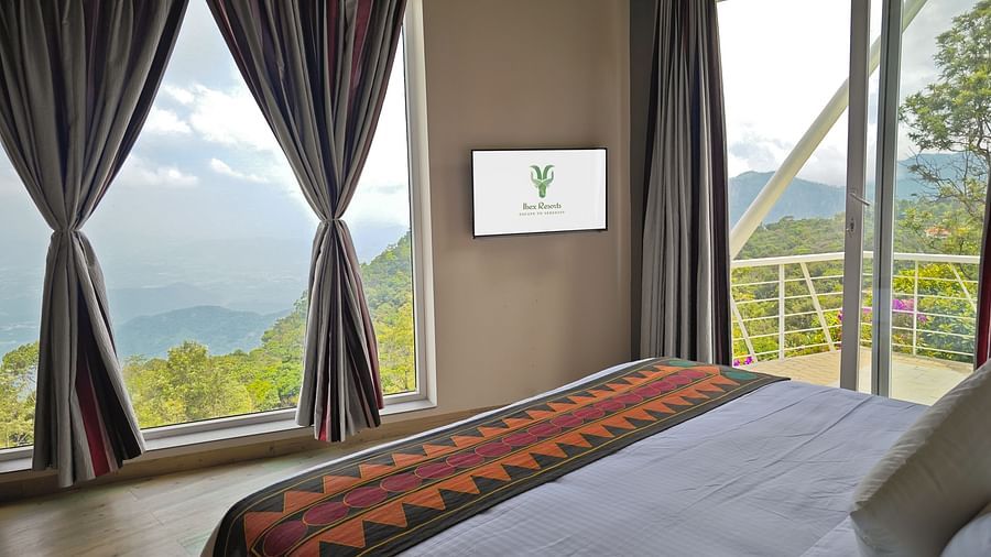 Outdoor seating area on a balcony with a wicker chair and scenic forest view at Ibex Resorts, Coonoor (Tapas).