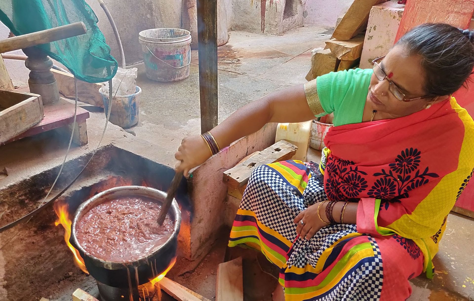 Woman stirring food in a large pot over an open fire.