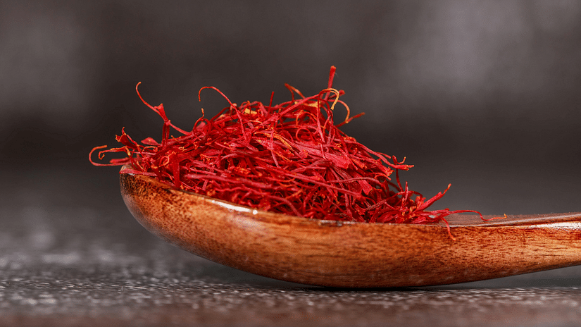 Red saffron threads piled in a wooden spoon, dark textured background, warm light