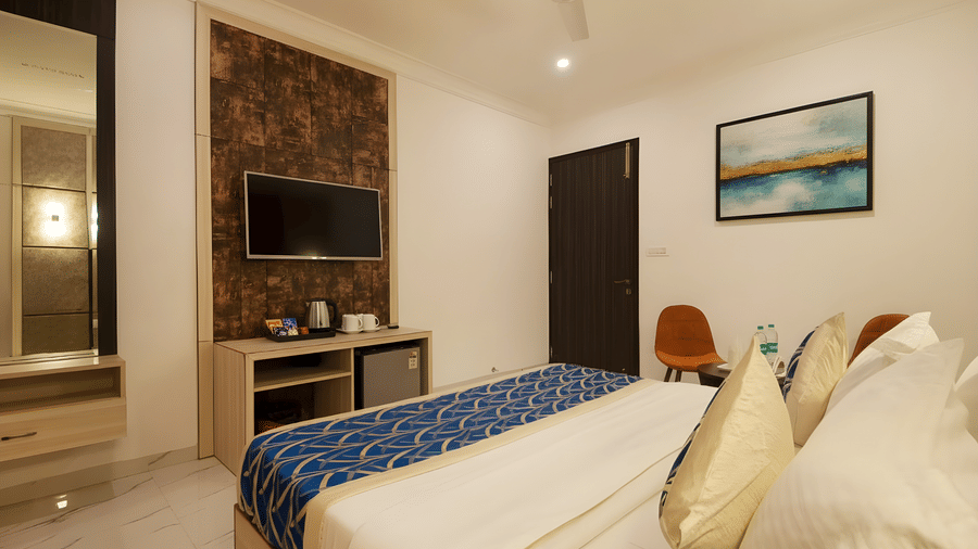A guest bedroom at Hotel Apple Park Delhi featuring a bed with a blue and gold patterned runner, a wall-mounted television, and a textured headboard panel.
