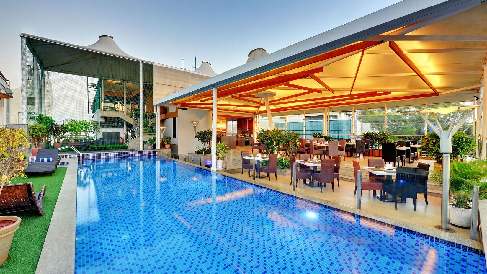 Outdoor dining area beside a rooftop pool at IRIS Hotel, Brigade Road, Bangalore, with modern seating and ambient lighting.