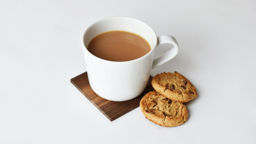 A coffee cup and saucer with cookies on a light-colored table.