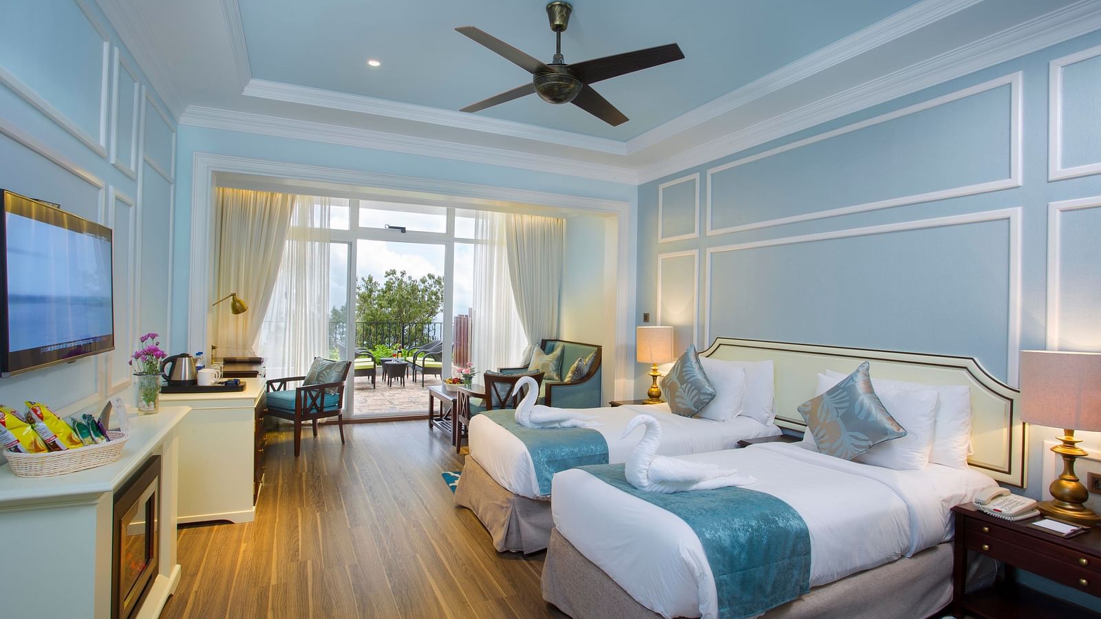 Twin beds with a side balcony view and a wall-mounted TV opposite the bed