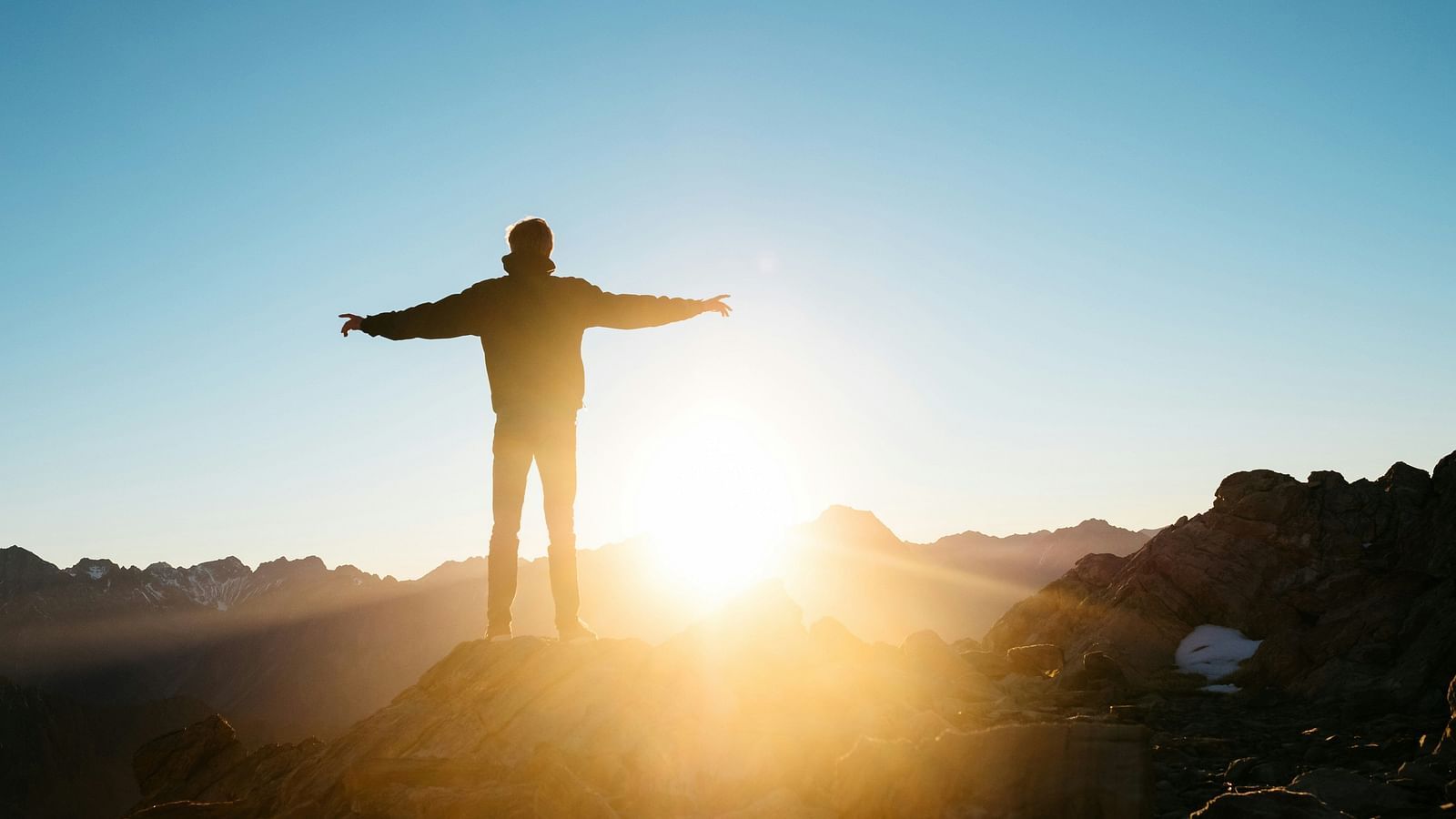 a person holding his arms out while looking at the sun rise in the distance