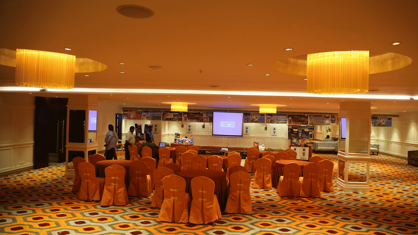 A warmly lit banquet hall with orange chairs arranged around tables - TGI Grand Fortuna, Hosur