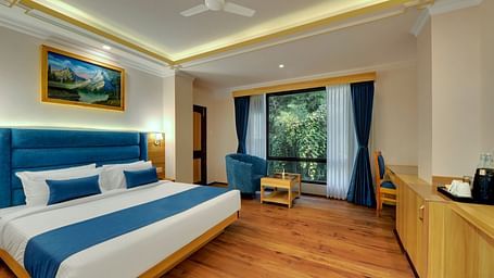 An image of a deluxe room with bed, sofa set, table, and an expansive window viewing the lush greenery - Yashshree Sikkim Blossom, Gangtok