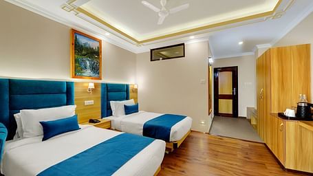 An image of family suite with twin beds, bed side tables, tea coffee maker, and paintings hung on the wall - Yashshree Sikkim Blossom, Gangtok