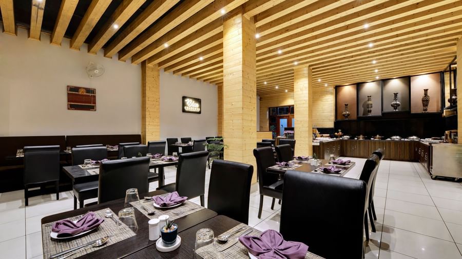 The Blue Charcoal Restaurant at the Sumitel Shangrila Deorali in Gangtok, with neatly set tables, black chairs, and a modern wooden ceiling design.