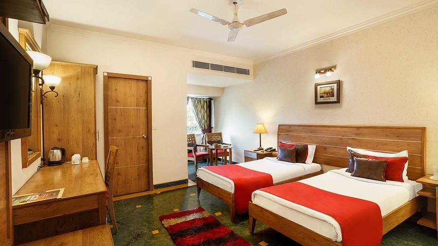 A twin bedroom featuring a floor mat, side tables, a mirror on the wall, and a small sitting area with two chairs