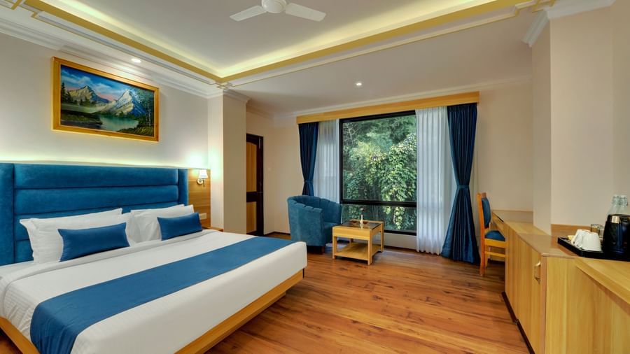 A deluxe room at Yashshree Sikkim Blossom in Gangtok with a queen-sized bed, a lounge chair and a table, a work desk, and an expansive window.