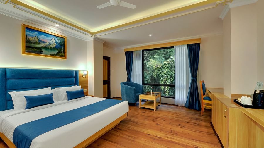 An image of a deluxe room with bed, sofa set, table, and an expansive window viewing the lush greenery - Yashshree Sikkim Blossom, Gangtok