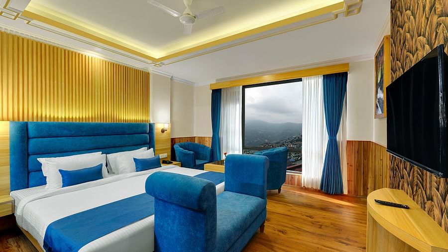 An image of the family suite at Yashshree Sikkim Blossom, Gangtok with a bed, a couch, a sofa set, a table, flat screen TV and an expansive window
