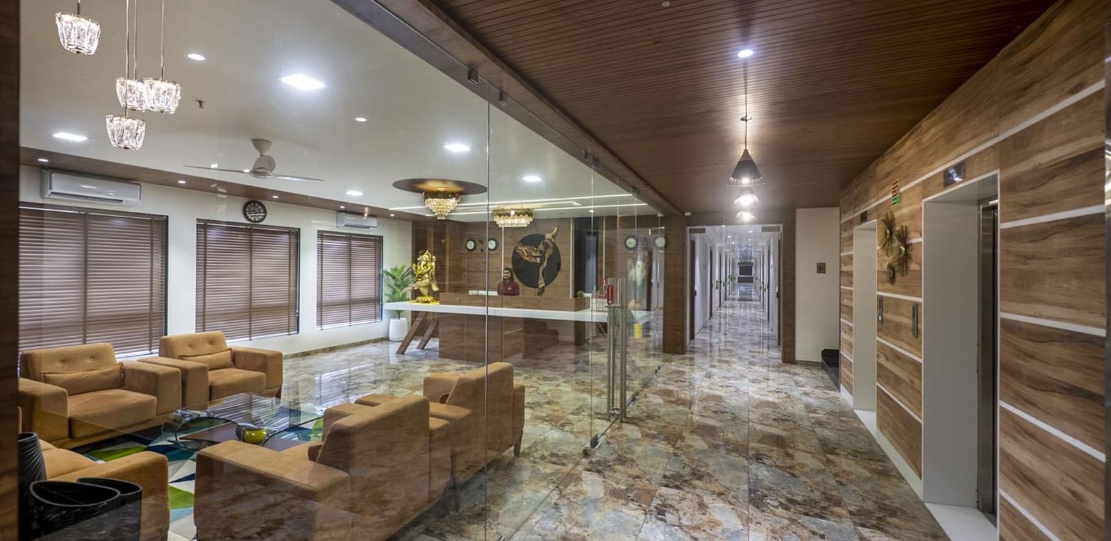 A lobby with armchairs and sofas arranged for seating, and a patterned floor leading to a reception area  at Angel Lords Eco Inn Amreli.