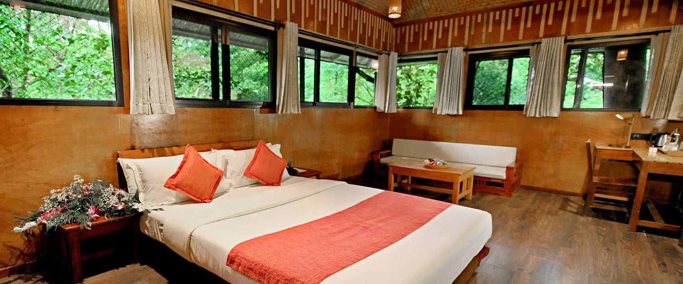 Room with multiple windows and a bed, offering lush forest views at Vythiri Resort, Wayanad