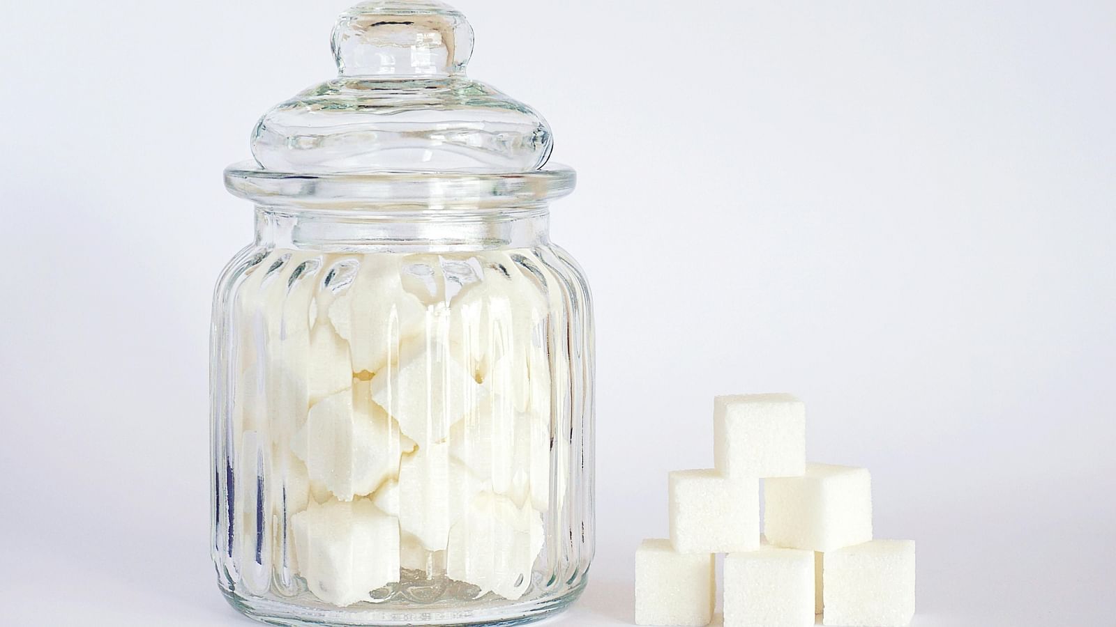 An image of a jar filled with sugar cubes, with a few cubes placed beside it on one side.