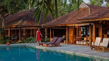 A shot of the swimming pool which also features lounge chairs, the restaurant, and palm trees in the background - BluSalzz Villas - Muhamma Resort, Alleppey
