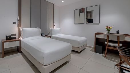 A well-lit Standard Room featuring two twin beds, a desk, and a chair. - The Pelican Hotel, Accra