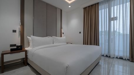 A modern and spacious Deluxe Room with a king size bed, sitting area, and large windows for natural light. - The Pelican Hotel, Accra