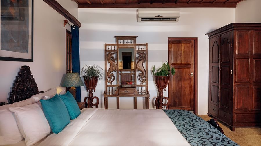 A shot taken from the side of the bed, with a wooden wardrobe and dress in the background - BluSalzz Villas - Muhamma Resort, Alleppey