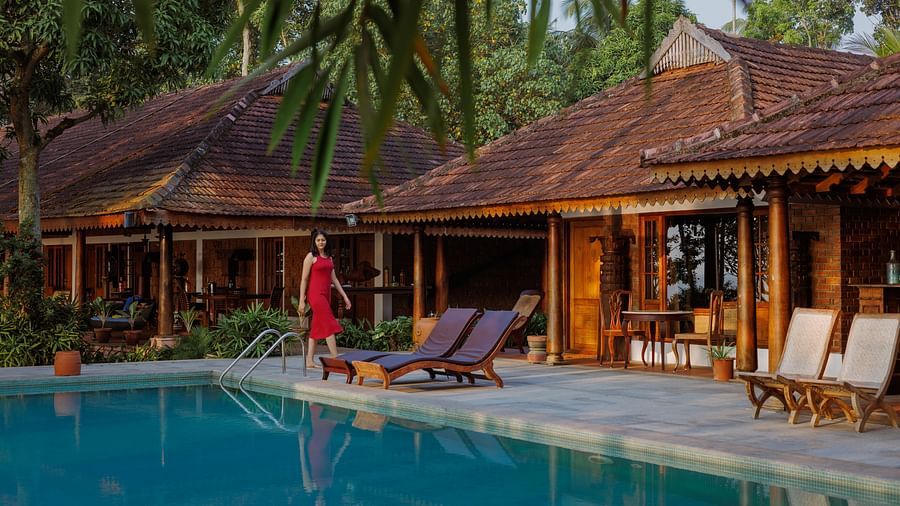 A shot of the swimming pool which also features lounge chairs, the restaurant, and palm trees in the background - BluSalzz Villas - Muhamma Resort, Alleppey
