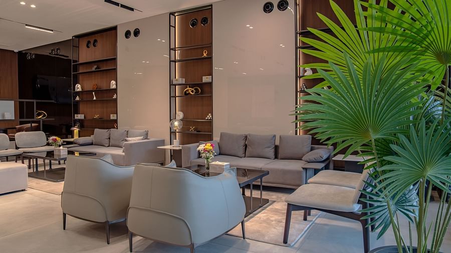 A well-lit living room with large windows, a variety of seating options, and potted plants.