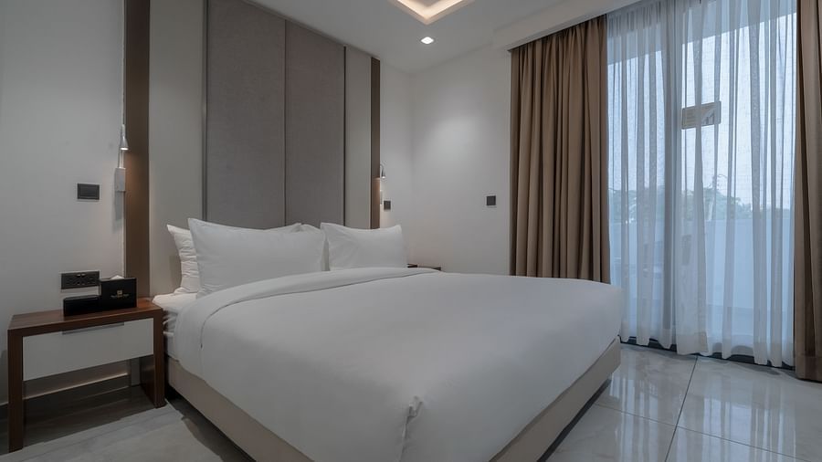 A modern and spacious Deluxe Room with a king size bed, sitting area, and large windows for natural light. - The Pelican Hotel, Accra