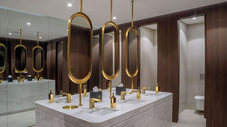 A modern bathroom with a marble countertop, double sinks, a circular mirror, and a separate toilet stall. - The Pelican Hotel, Accra