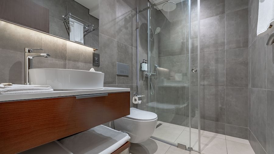 Modern Standard Room bathroom with glass shower, vessel sink, wooden vanity, soft lighting, and sleek fixtures. - The Pelican Hotel, Accra