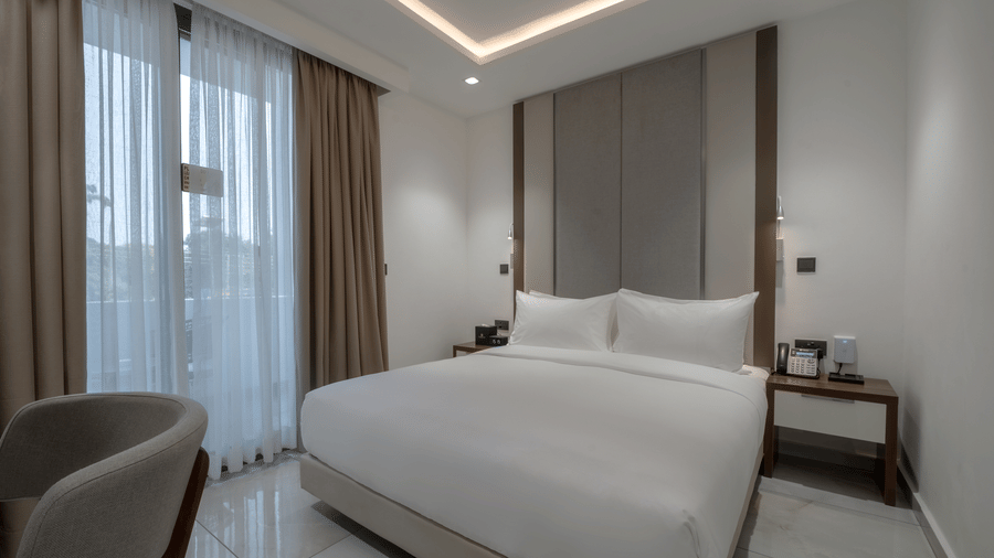 A modern Junior Suite with a large king size bed near a large window at The Pelican Hotel, Accra. 
