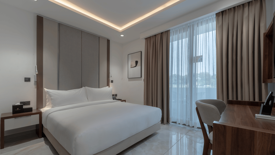 Standard Room with king size bed, soft lighting, wooden desk, large window, and cozy ambience. - The Pelican Hotel, Accra