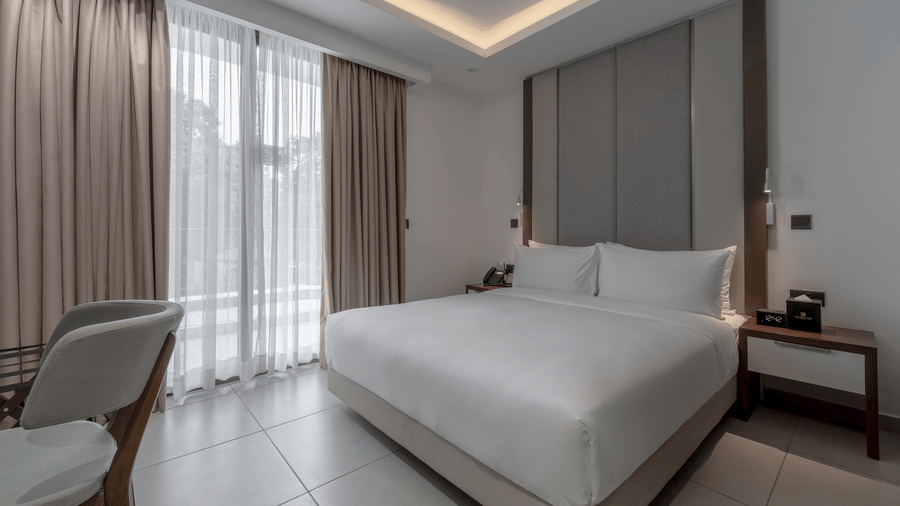 One of the Premier Suites in Accra featuring a plush bed with patterned headboard under warm lighting next to a doorway to the private balcony at The Pelican Hotel, Accra
