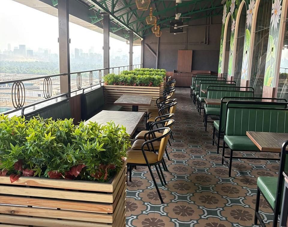 An outdoor seating area with tables and chairs is visible, featuring plants and a view of the surroundings - Melior Inn