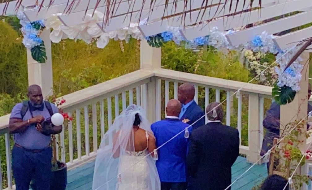 A bride walking down a wooden deck outdoors with guests present on either side | A Stone's Throw Away