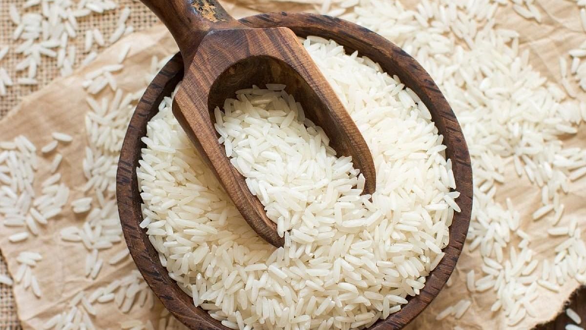 A wooden scoop filled with IR-64 rice placed on a piece of burlap and surrounded by scattered grains.