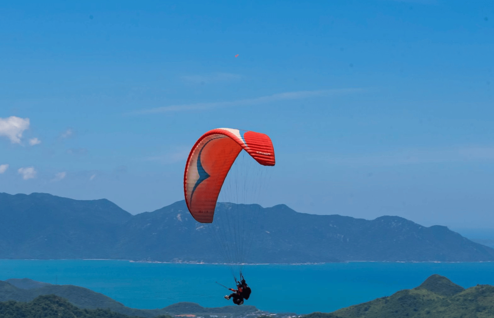 Paraglider soaring over forested hills and blue waters, enjoying scenic coastal