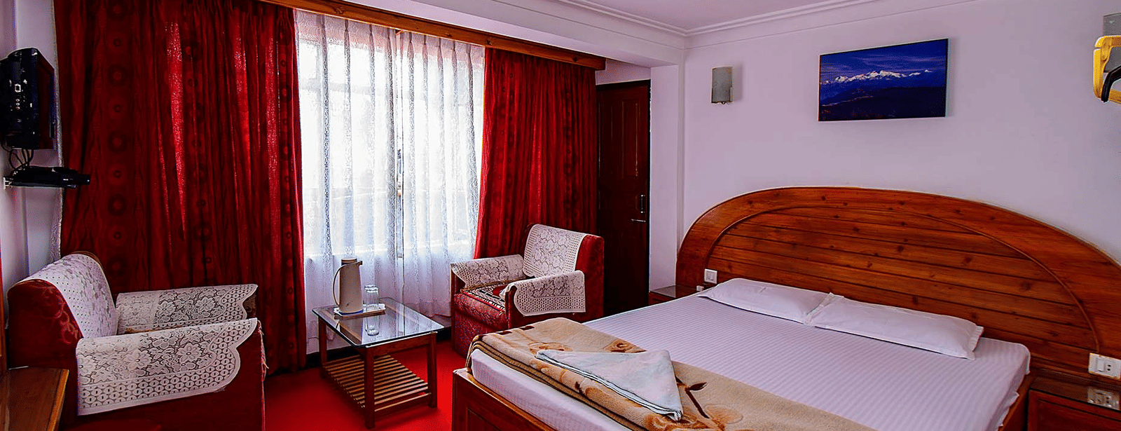 Hotel bedroom featuring a double bed, red carpet, white walls, and a small sitting area with patterned chairs at Hotel Dolphin Darjeeling.
