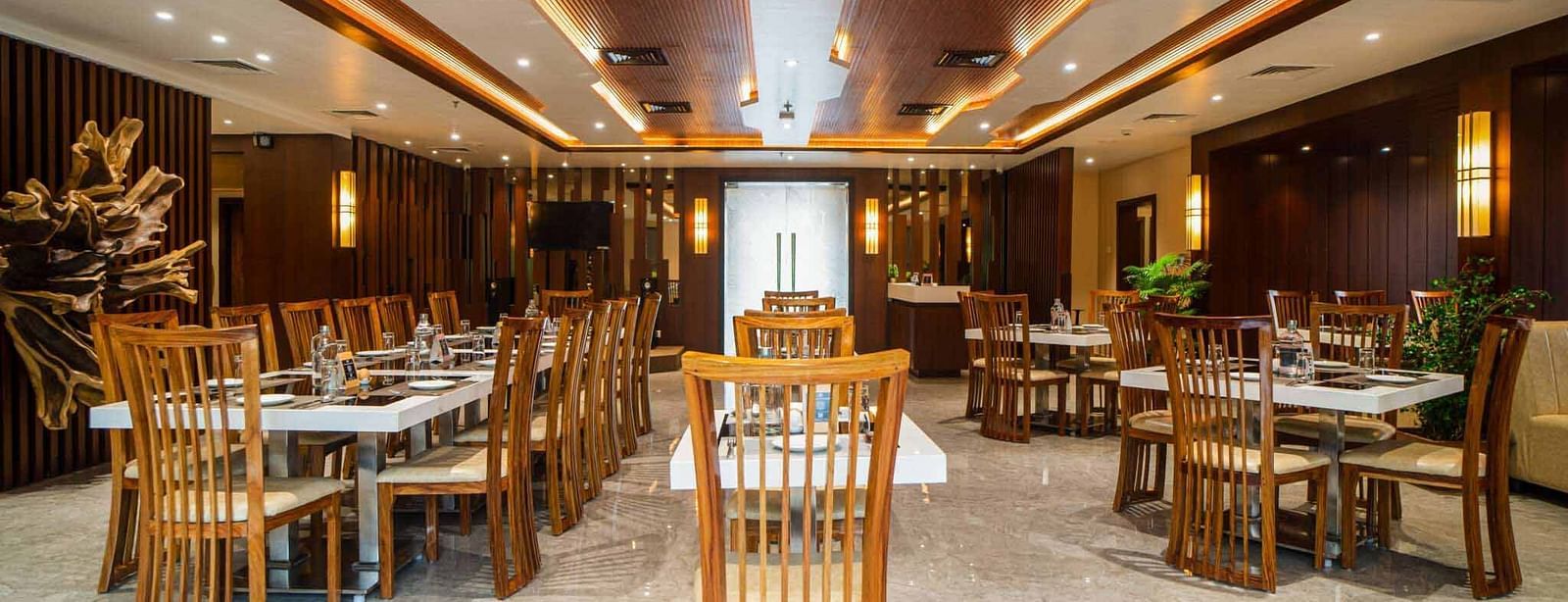 The spacious dining hall at Mansha Palace is furnished with numerous set tables and comfortable wooden seating.