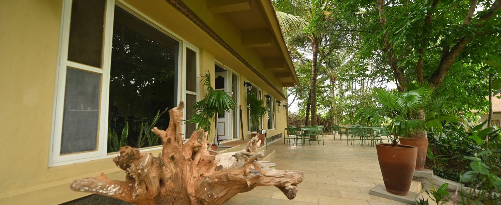 Fireflies Resorts exterior with a tiled walkway, potted plant, and large wooden log decor placed beside glass windows under a yellow roof.