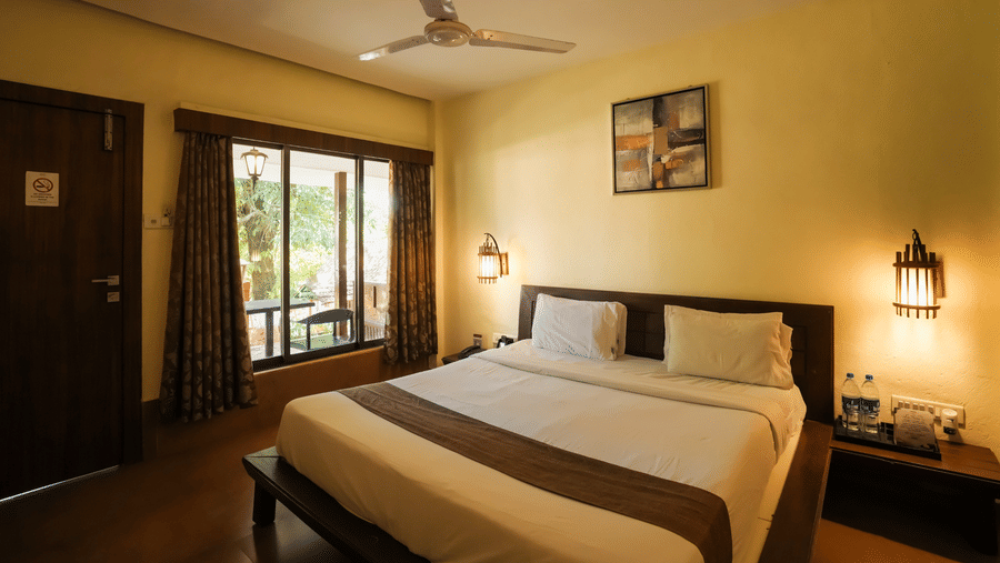 A well-appointed bedroom at Adamo The Village featuring a large bed, window seating, and warm ambient lighting.