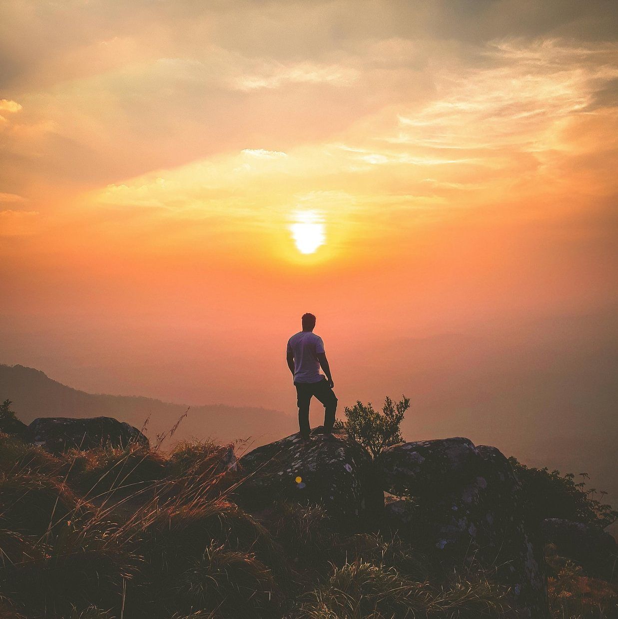 Silhouette of a person standing on a mountaintop during a vibrant orange sunset.