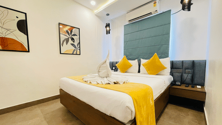 Double bed room at Hotel Kyzen Smart Stays Madhapur featuring a king bed with yellow and white bedding, teal headboard panel, framed artwork, and warm ceiling lighting.