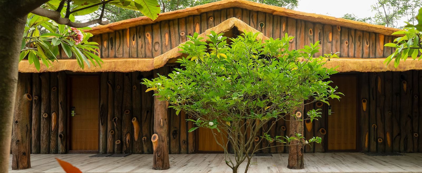 A wooden building with a thatched roof, surrounded by trees and plants, suggests a natural or rustic setting | Standard Room | RD's Nature Retreat, Bangalore